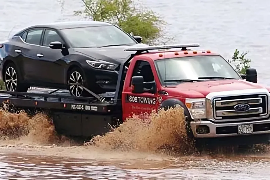 A red 808 Towing tow truck towing a black car through a flooded area